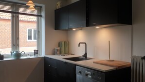 A modern kitchen with a window, black cabinets, a sink, and a radiator. - Køge Guesthouse (Koge)