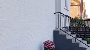 A building with a white exterior, a black staircase, and two large potted plants with pink flowers. - Køge Guesthouse (Koge)