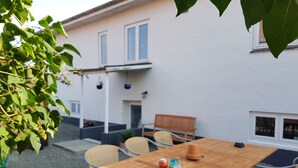 A wooden table with chairs in a courtyard, a bench, and a hanging plant. - Køge Guesthouse (Koge)