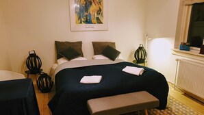A hotel room with a bed, a bench, a nightstand, a lamp, and a painting on the wall. - Køge Guesthouse (Koge)
