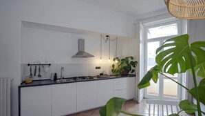 A modern kitchen with white cabinets, a black countertop, a gas stove, a stainless steel range hood, and a large window with a view of the outside. - Casa Giada (Salerno)