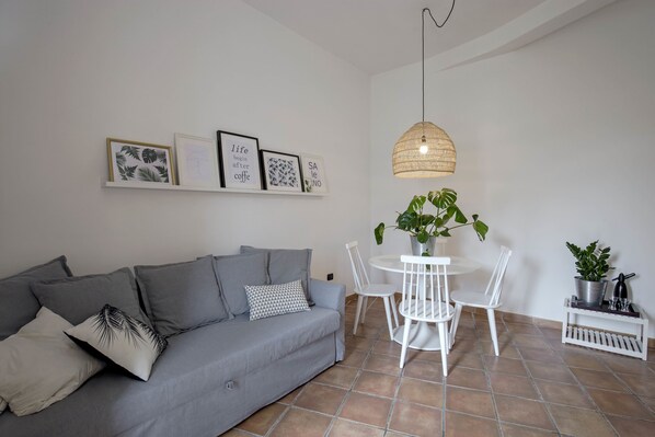 A living room with a grey sofa, white chairs, a round table, and a hanging light fixture. - Casa Giada (Salerno)