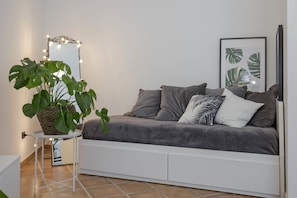 A modern living room with a grey sofa, a small side table with a plant, a mirror with lights, and a framed plant artwork on the wall. - Casa Giada (Salerno)