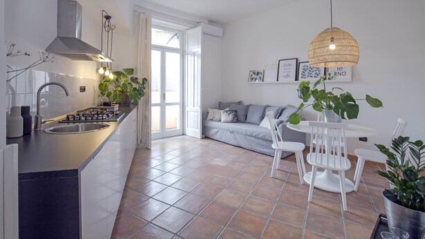 A modern kitchen with a central island, a dining area with white chairs, and a sofa in the background. - Casa Giada (Salerno)