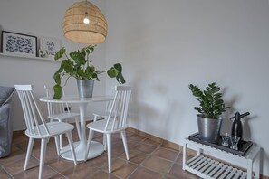 A dining area with a round table and white chairs, a potted plant, a hanging light fixture, and a small shelf with a bottle and glasses. - Casa Giada (Salerno)