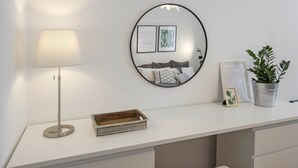 A white desk with a lamp, a mirror, framed pictures, a plant, and a wicker basket. - Casa Giada (Salerno)