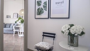 A modern interior with a white sofa, a dining table with chairs, a small black chair with a geometric pillow, and a vase with white flowers on a white table. - Casa Giada (Salerno)