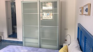 A bedroom with a bed, a wardrobe, a bathroom with a shower, and a view of buildings outside. - Sole Flat (Minori)