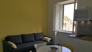 A compact living space with a sofa, a dining table, chairs, a window, and a microwave. - Sole Flat (Minori)