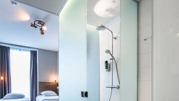 Une chambre d’hôtel moderne avec deux lits, un espace douche et une cloison en verre.