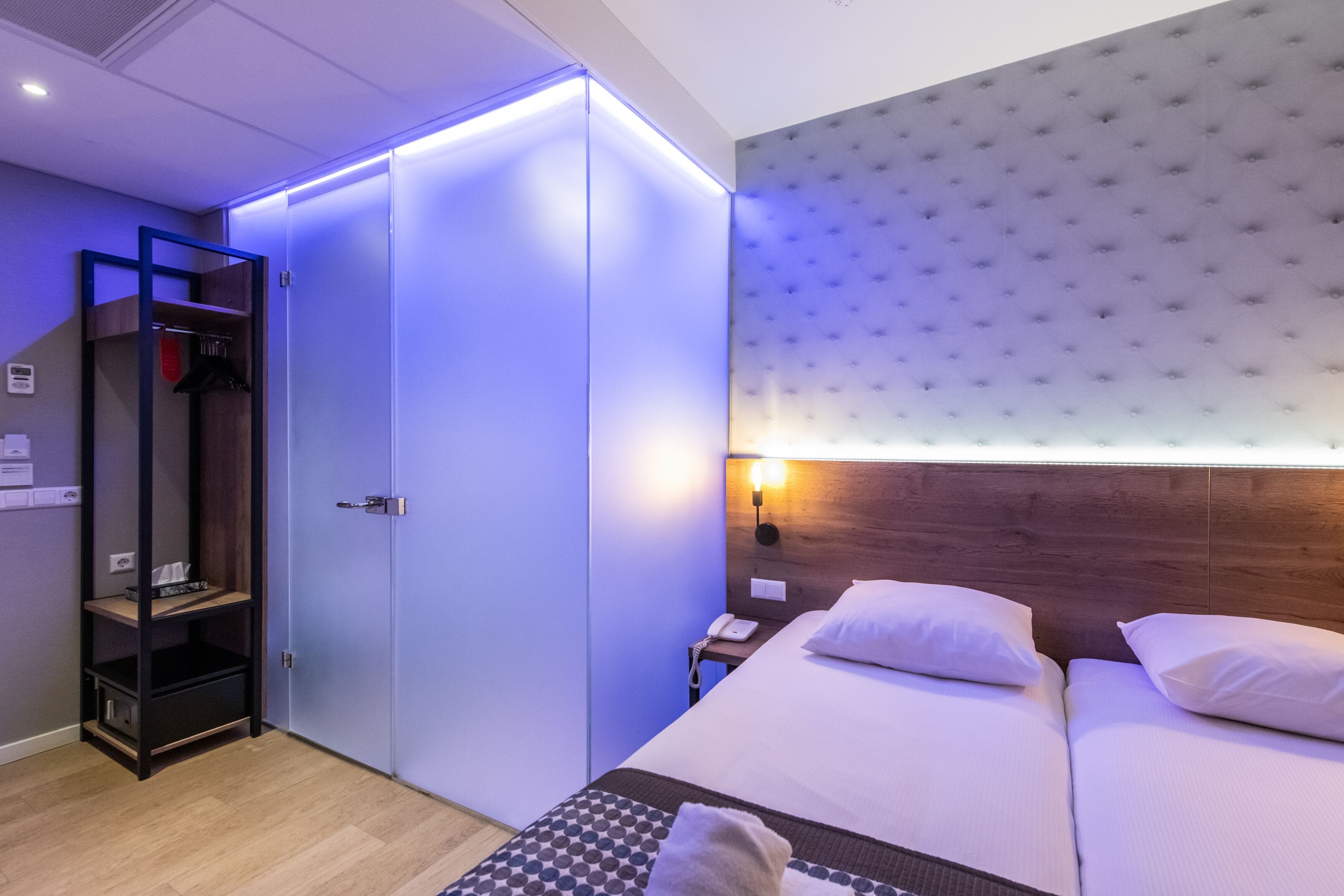 Une chambre d’hôtel comprenant un lit, une armoire, une étagère et un luminaire fixé au mur.