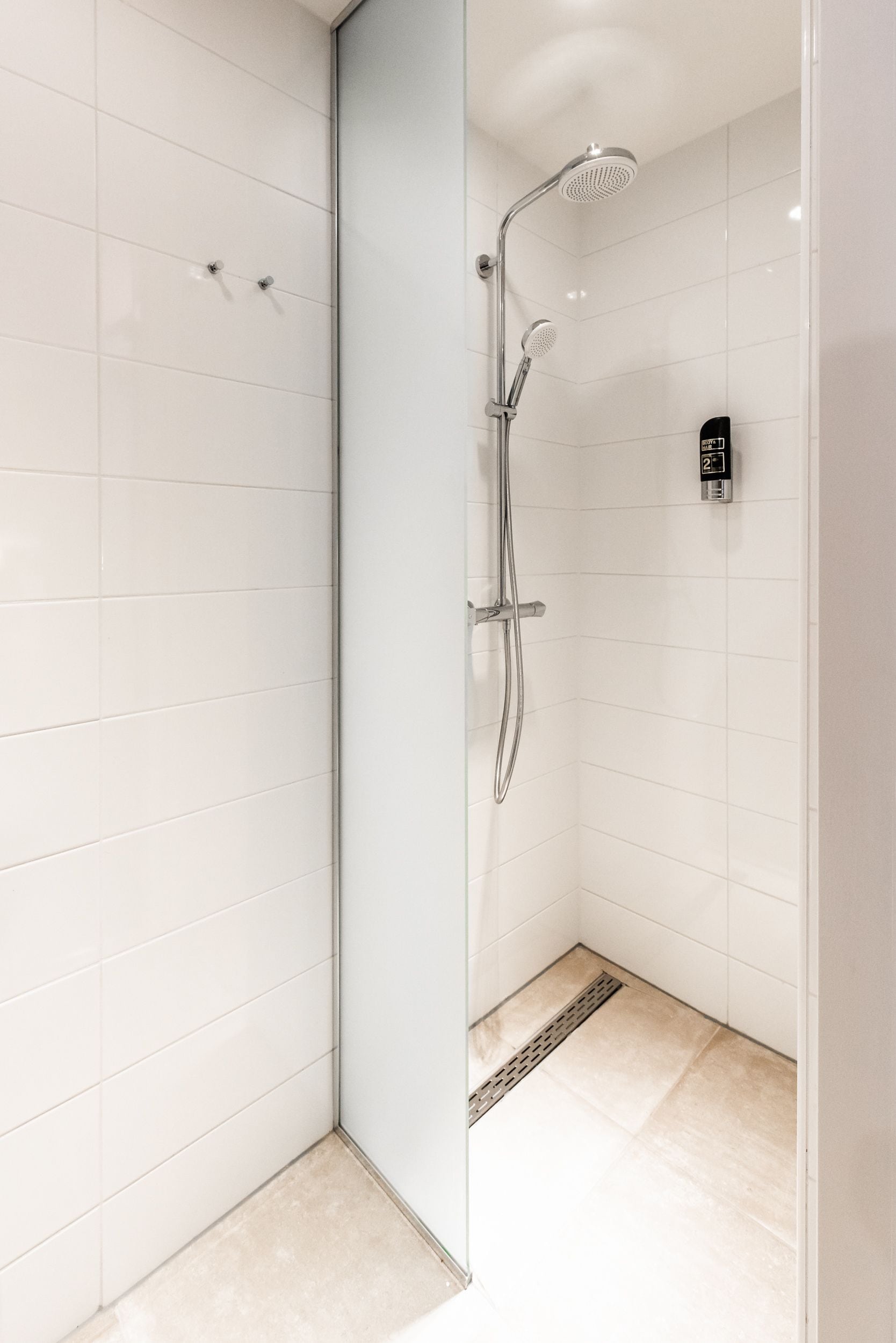 A modern shower with a handheld showerhead and a wall-mounted rain showerhead, a control panel, and a tiled floor.