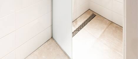 A modern shower with a handheld showerhead and a wall-mounted rain showerhead, a control panel, and a tiled floor.