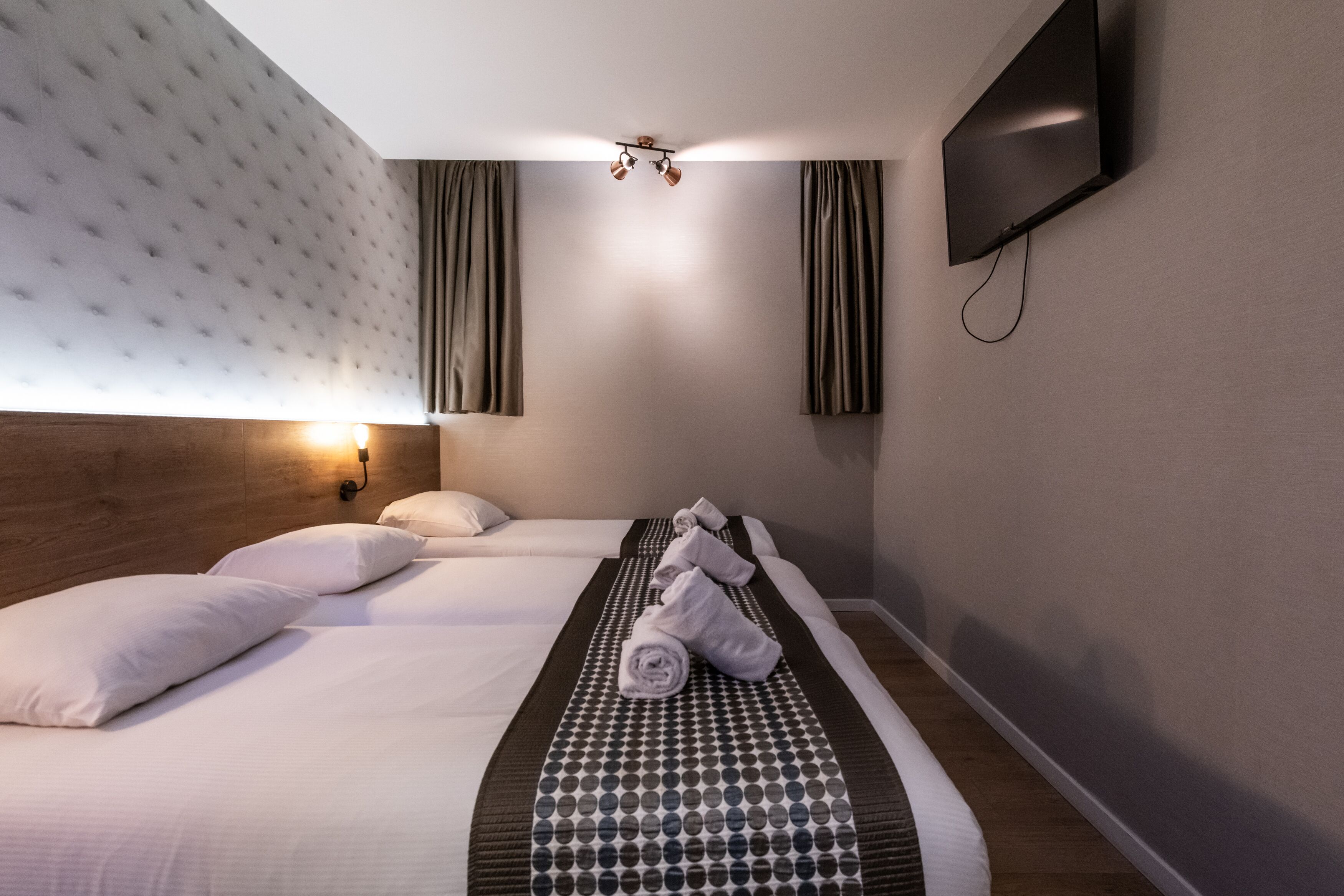 Une chambre d’hôtel avec un grand lit, un téléviseur fixé au mur et une tête de lit dotée d’un luminaire.