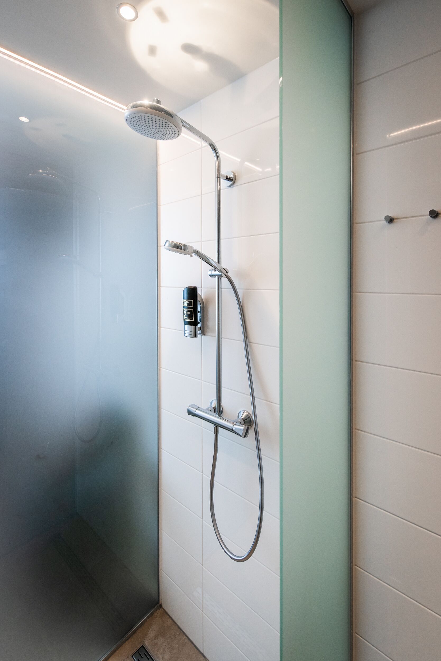 A modern shower with a handheld showerhead, a handheld shower attachment, and a wall-mounted control panel.