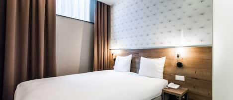 A hotel room with a large bed, a wooden headboard, a bedside table with a phone, and curtains.