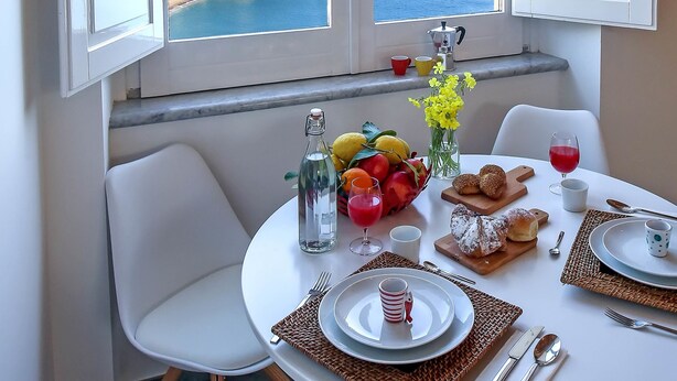 A dining area with a table set for two, a view of the sea, and a window with white shutters. - Castello Mezzacapo by Starhost (Scala)