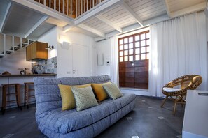 Una sala de estar moderna con un sofá, una silla de mimbre, una zona de cocina y una escalera.