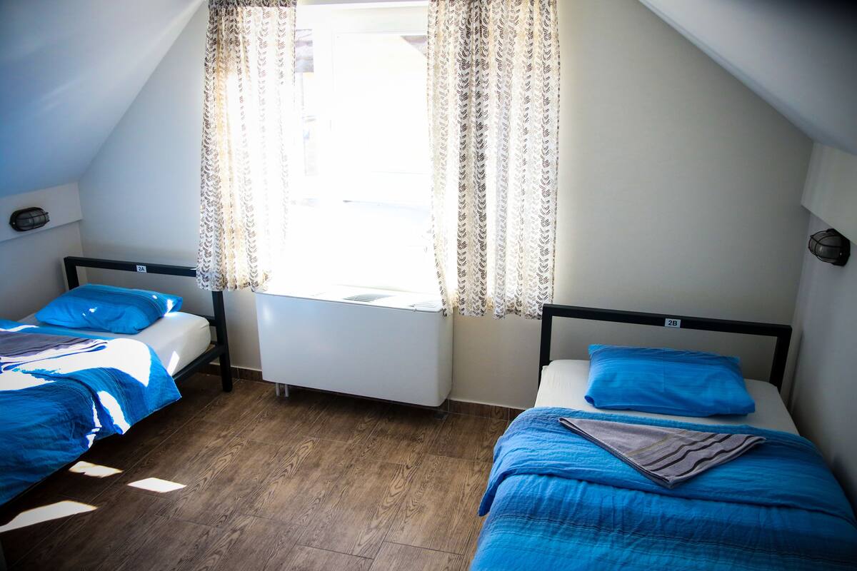 Quarto com duas camas, um radiador e uma janela com cortinas.