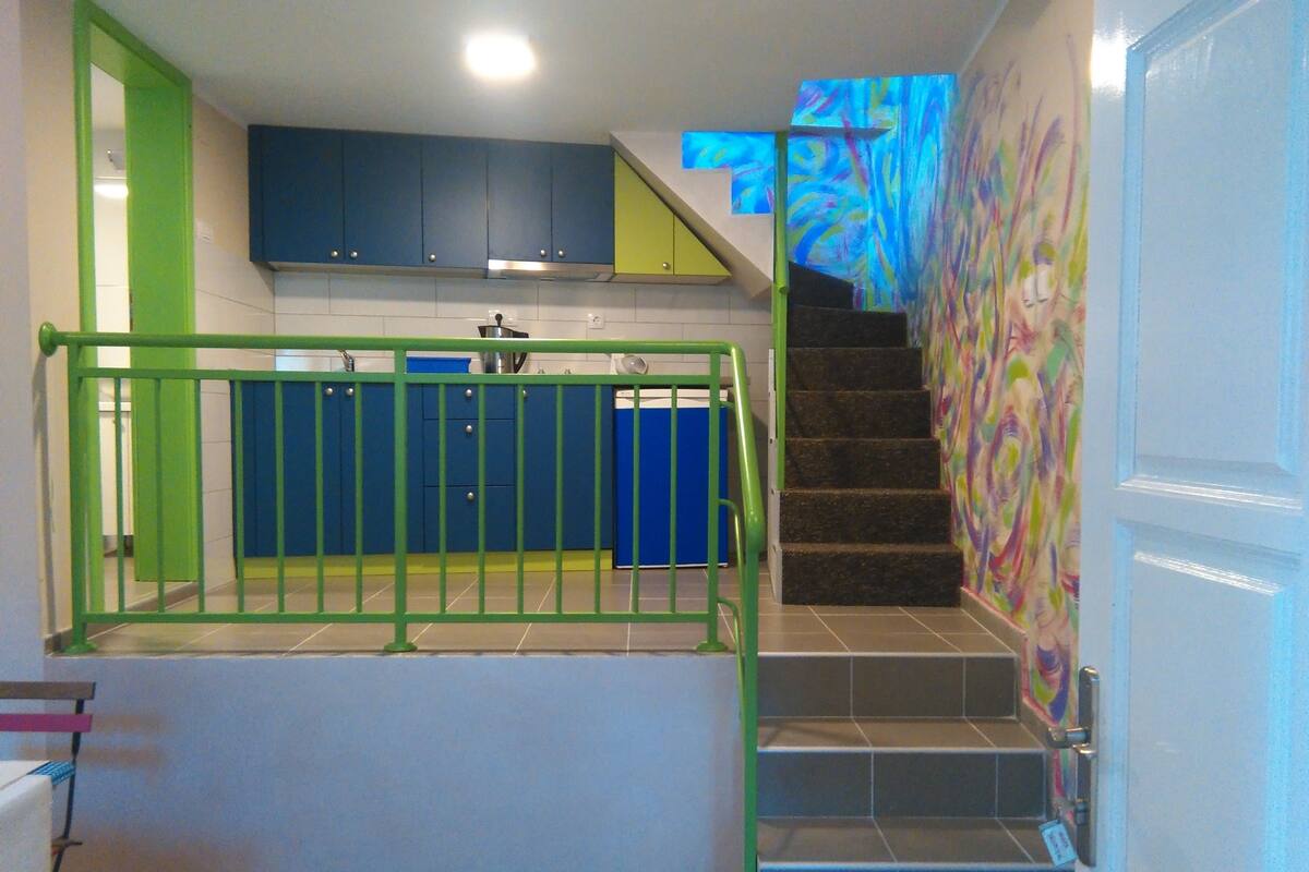 Uma escadaria com corrimão verde que leva a uma área de cozinha com armários azuis.