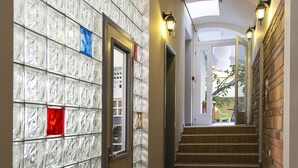 A hallway with a glass block wall, a staircase, and a door leading to an elevator. - Varad Inn Hostel and Cafe (Novi Sad)