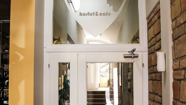 A hotel entrance with a glass door, a coat rack with an umbrella, and a sign reading "RADINN hotel & cafe". - Varad Inn Hostel and Cafe (Novi Sad)
