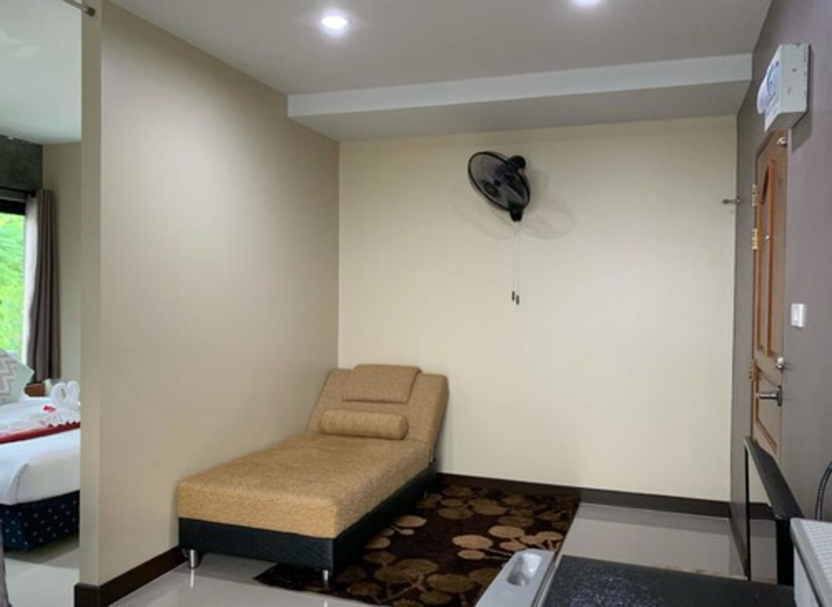 A small room with a single bed, a massage chair, and a fan on the wall.