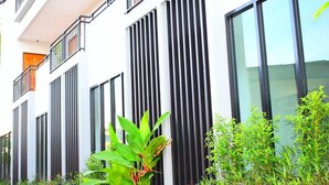 Un edificio moderno con listones verticales negros en la fachada, balcones y abundante vegetación al frente.