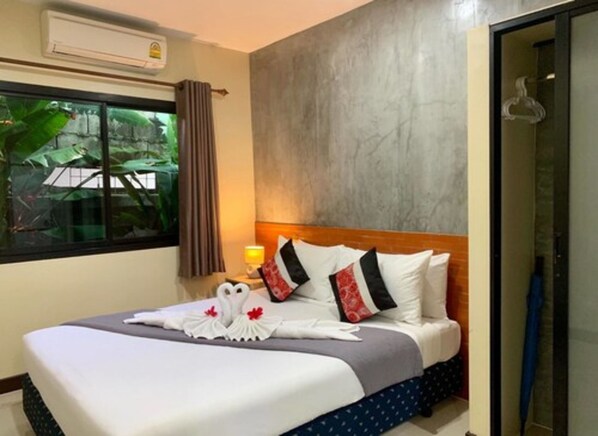 Habitación de hotel con cama, ventana con cortinas, mesita de noche con lámpara y vista a zonas verdes.