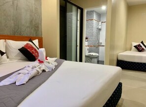 Habitación de hotel con una cama bien hecha, baño con ducha y una pequeña zona de estar.