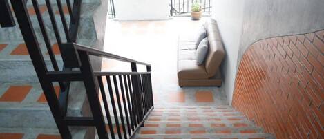 Un escalier avec une rampe noire menant à un balcon où se trouvent un canapé et un pot de fleurs.