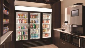 Una kitchenette equipada con un refrigerador lleno de bebidas y aperitivos, un microondas y una cafetera.