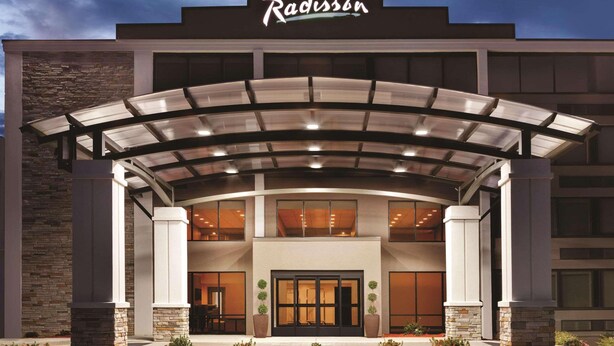 Un hotel Radisson con un diseño moderno, que cuenta con una entrada cubierta, fachada de piedra y grandes ventanales.