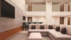 Un moderno vestíbulo de hotel con un amplio sofá modular, un televisor de pantalla plana y un comedor con techo alto y ventanas grandes.