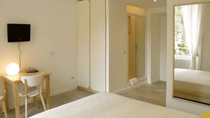 A bedroom with a bed, a desk with a chair, a TV mounted on the wall, and a large window with curtains. - Il Sampietrino dei Cavalleggeri B&B (Rome)