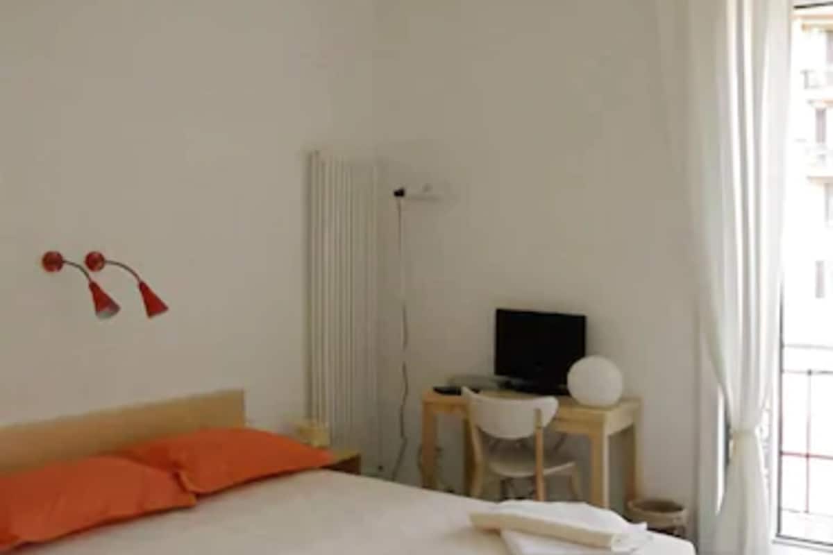A bedroom with a wooden bed, a desk with a computer, and a radiator.