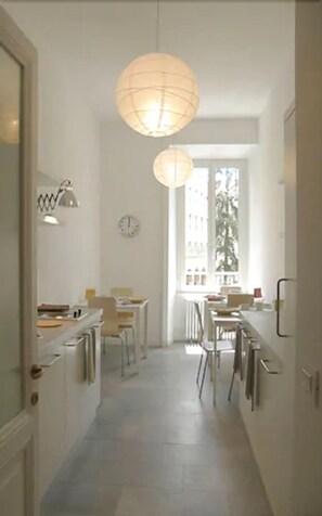 A narrow hallway with a dining area at the end, featuring a large window with a view of buildings. There are two pendant lights hanging from the ceiling. - Il Sampietrino dei Cavalleggeri B&B (Rome)