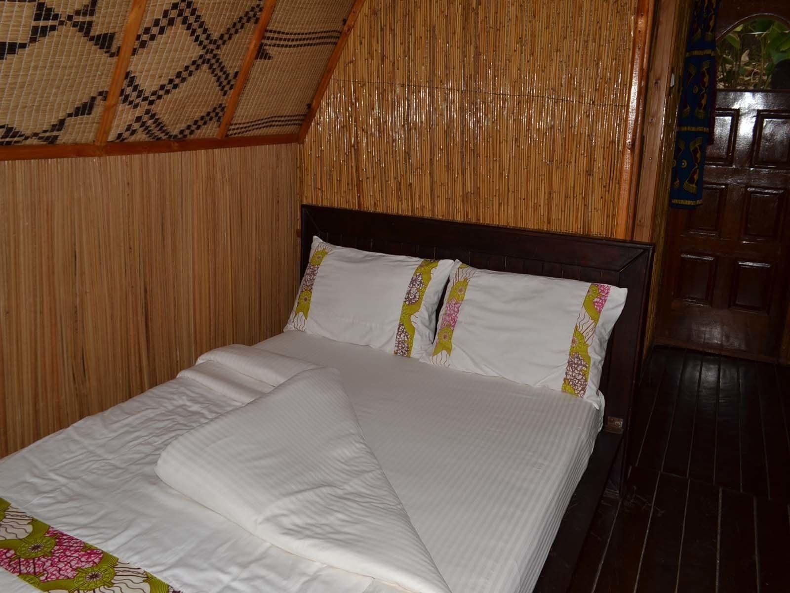 A bed with white bedding and decorative pillows, a wooden headboard, and a bamboo wall panel.