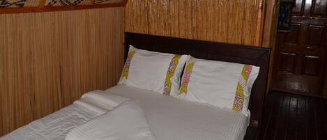 Una cama con ropa de cama blanca, almohadas decorativas, un cabecero de madera y un panel de pared de bambú.
