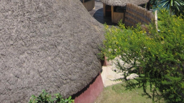 Thatched-roof huts with wooden benches, overlooking a calm lake and lush greenery. - Rwiza Village (Mubuga)