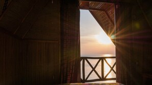 A room with a bed, a wooden ceiling, and a view of the sea through an open door. - Rwiza Village (Mubuga)