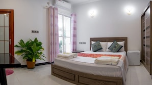 A bedroom with a wooden bed, a bedside table, a potted plant, and a window with curtains. - Athiriveli (Thoddoo)