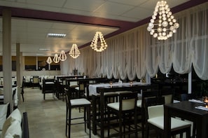 Un ristorante con diversi tavoli e sedie, tovaglie bianche e luci decorative appese.