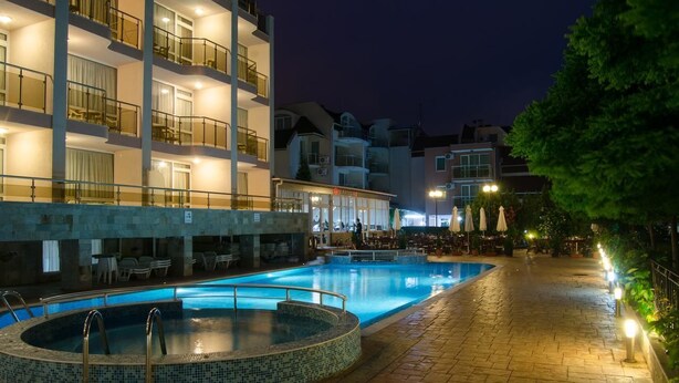 A swimming pool area with a hot tub, outdoor seating, and a building with balconies in the background. - Tropics Hotel (Sveti Vlas)