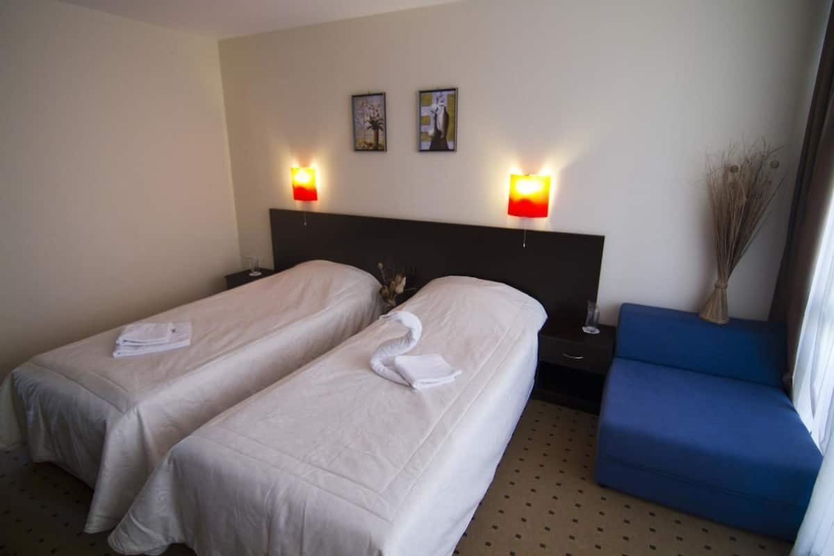 A hotel room with two single beds, a nightstand, a blue armchair, and two wall-mounted lamps.