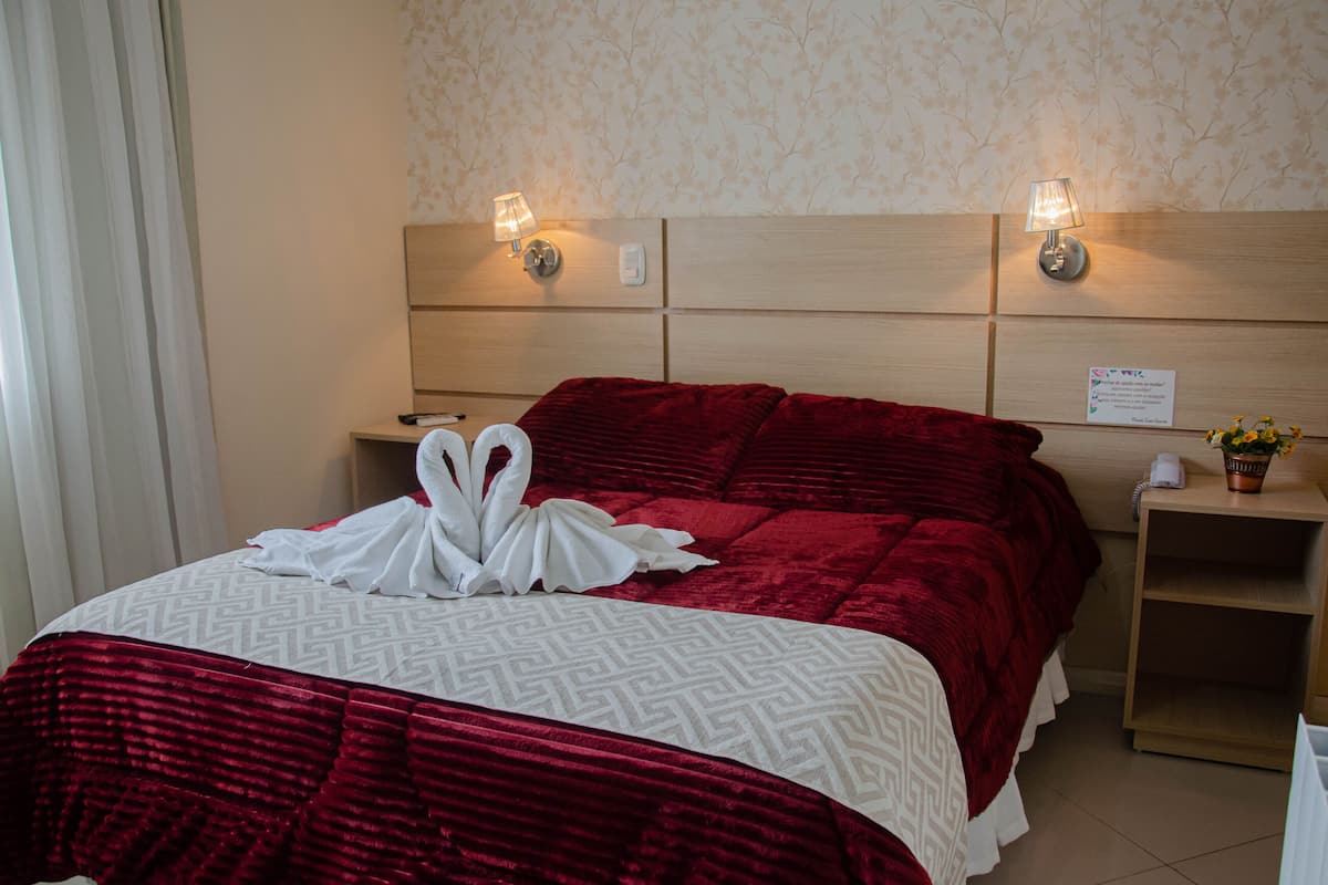 Hotellihuone, jossa on suuri sänky, kaksi yöpöytävalaisinta, yöpöytä, jossa on puhelin, ja pieni huonekasvi.