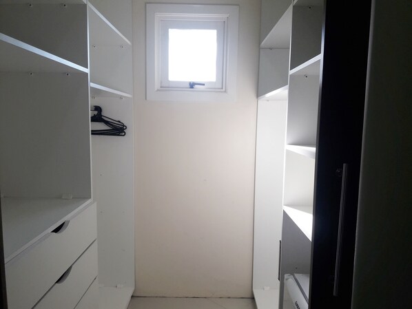 A walk-in closet with white shelving units and a small window at the top. - Pousada Lanai (Gramado)