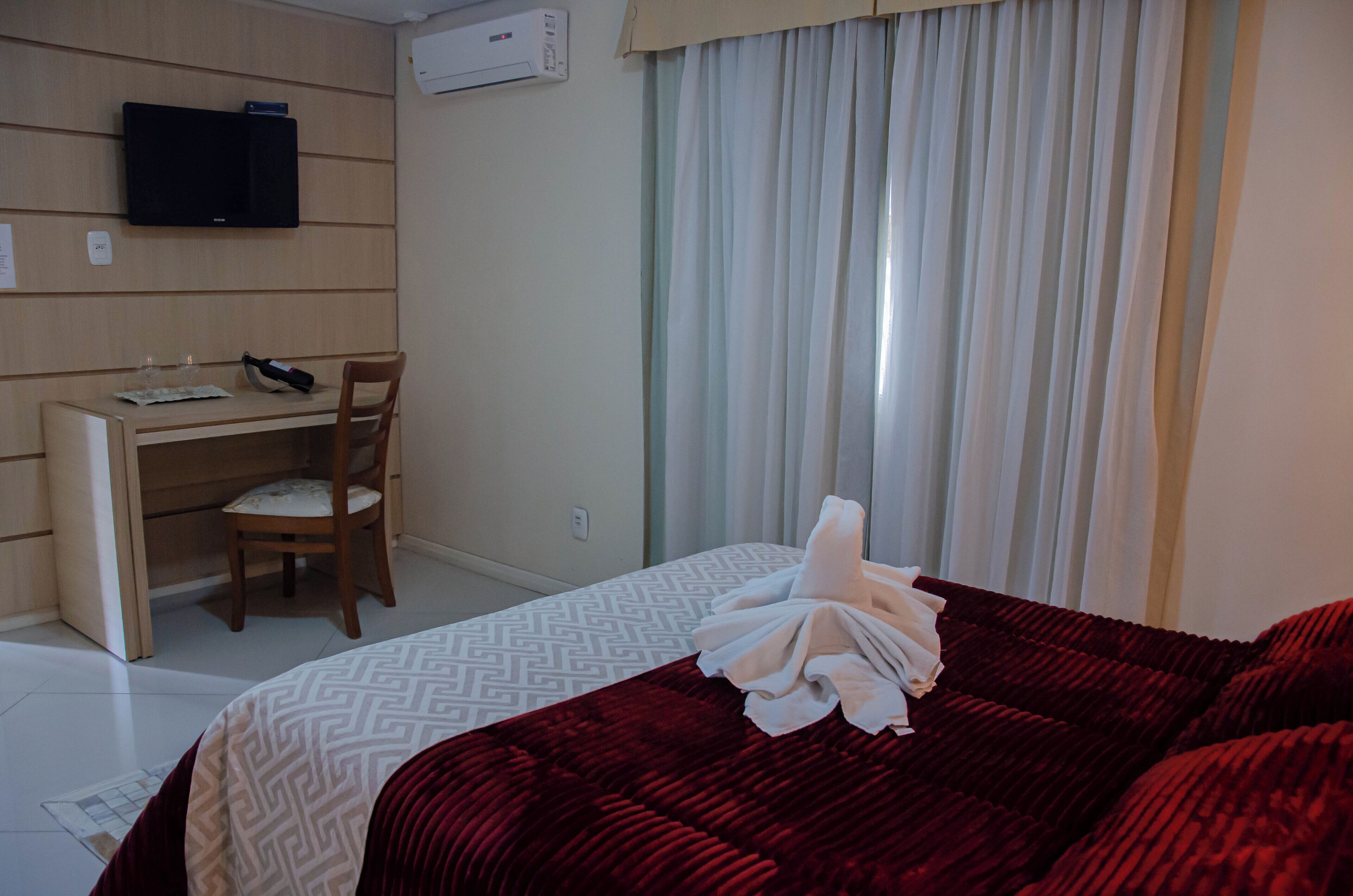 Une chambre d’hôtel avec un lit, un bureau, une chaise, une télévision et une fenêtre avec des rideaux.