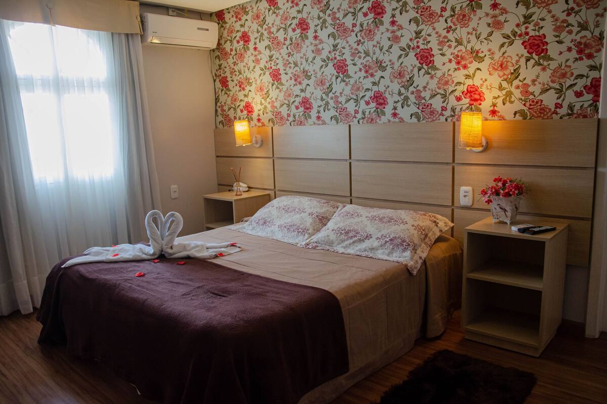 Hotellihuone, jossa on suuri sänky, kukallinen tapetti, yöpöytälamput ja yöpöytä, jossa on kaukosäädin.