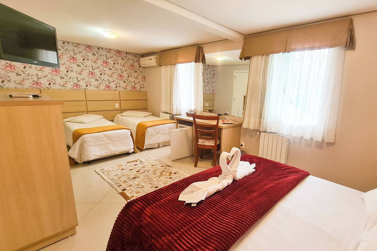 Hotellihuone, jossa on kaksi sänkyä, työpöytä, tuoli, televisio ja ikkuna, jossa on verhot.